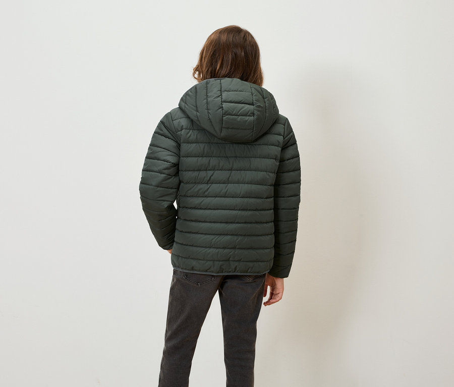 Zozadu je vidieť osoba s hnedými vlasmi v zelenej páperovej bunde s kapucňou a sivých džínsoch.