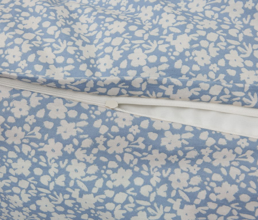 Detail látky s modrým podkladom a bielym kvetinovým vzorom, doplnené o biely zips.