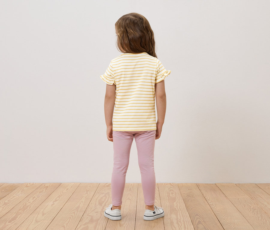 Dievča stojí chrbtom, má na sebe žlto-biely pruhovaný top s volánikmi, ružové legíny a biele tenisky.