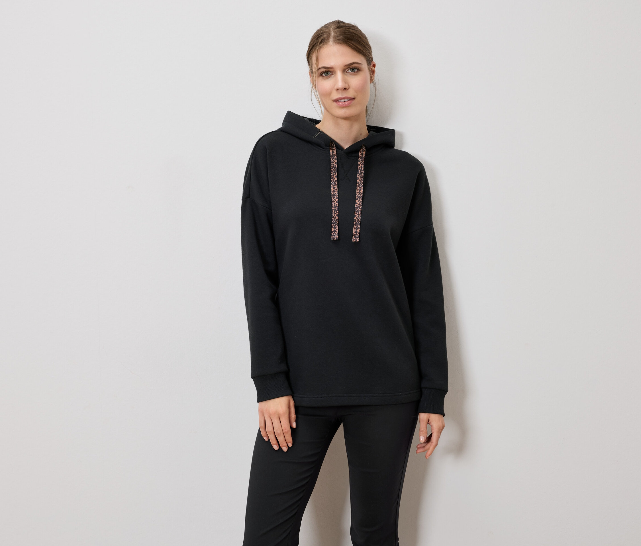 Žena má na sebe čiernu mikinu s kapucňou a nohavice.