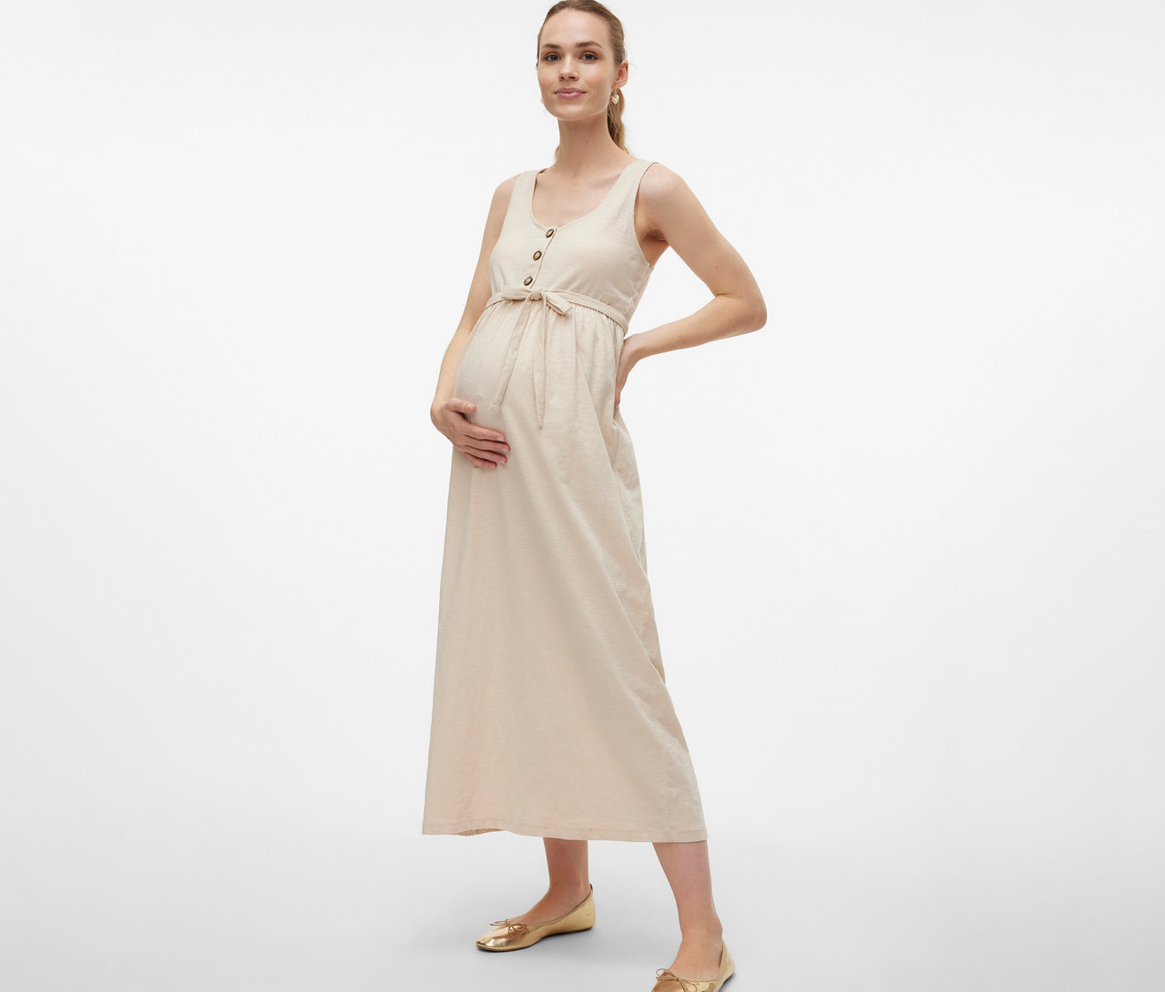 Tehotná žena v tehotenských šatách MAMALICIOUS »MLEVI LIA« s opaskom a gombíkmi pózuje s rukami na bruchu a boku.