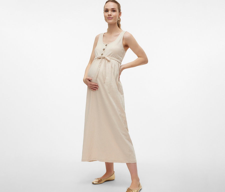 Tehotná žena v tehotenských šatách MAMALICIOUS »MLEVI LIA« s opaskom a gombíkmi pózuje s rukami na bruchu a boku.