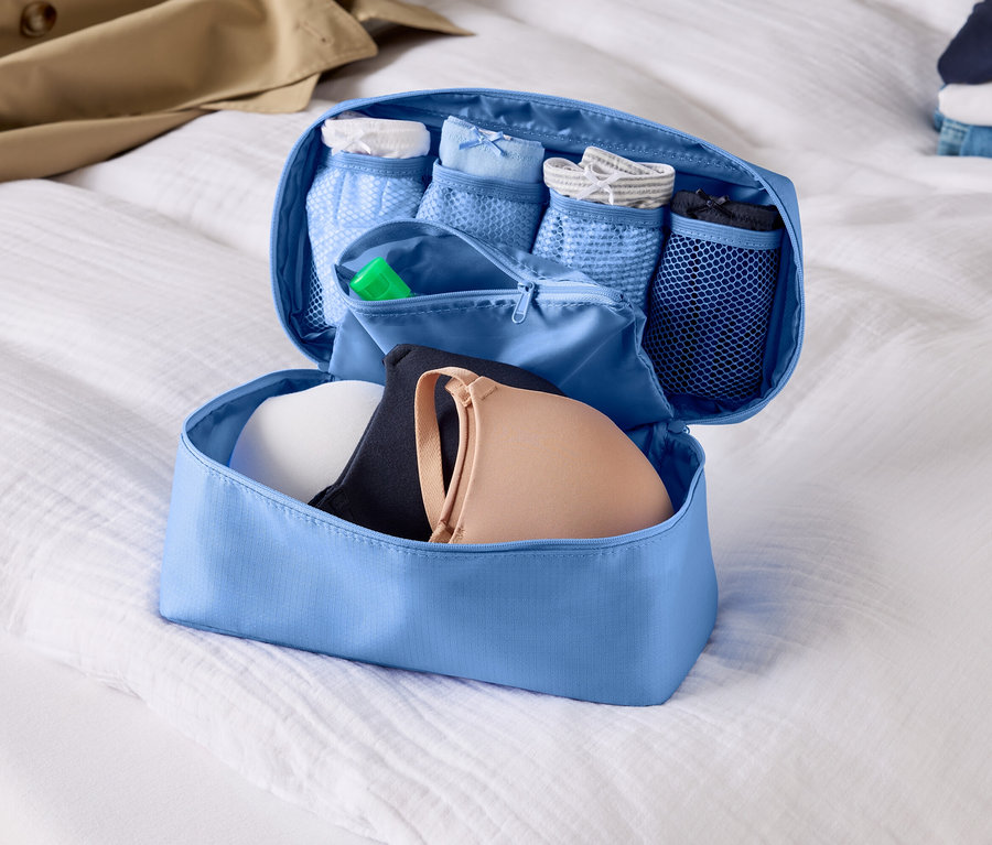 Otvorený, svetlomodrý organizér batožiny s podprsenkami a spodnou bielizňou na bielej plachte.