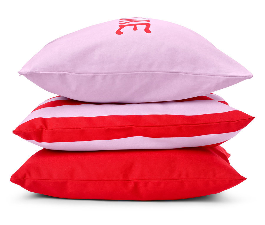 Tri vankúše sú naskladané: ružový vankúš s nápisom, červeno-biely pruhovaný vankúš a červený vankúš.
