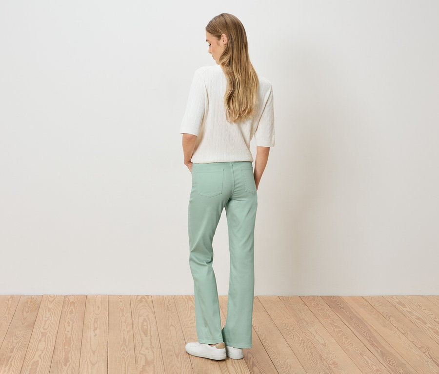 Pohľad zozadu na ženu s blond vlasmi v bielom svetri a svetlozelených nohaviciach.