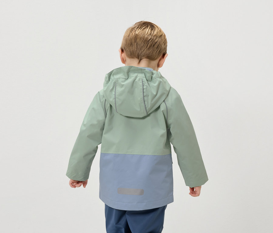 Pohľad zozadu na dieťa s blond vlasmi v dvojfarebnej bunde zelenej a modrej farby.