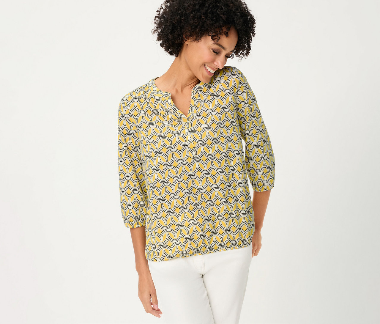 Usmievavá sa žena v 3/4 blúzkovej košeli Olsen so žltým vzorom a bielych nohaviciach.