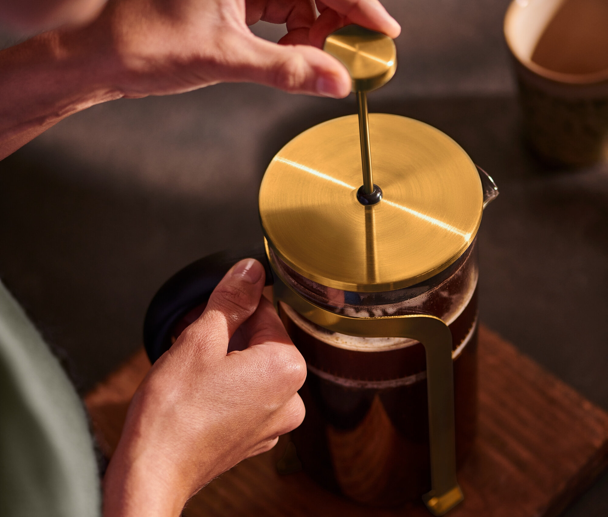 Osoba stláča zlatú kanvicu french press 800 ml na 6 šálok na drevenom podklade.