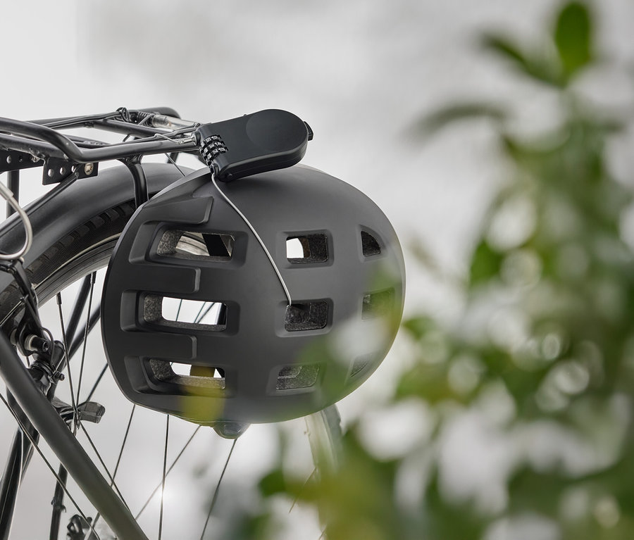 Čierna cyklistická prilba visí so zámkom na batožinovom nosiči bicykla.