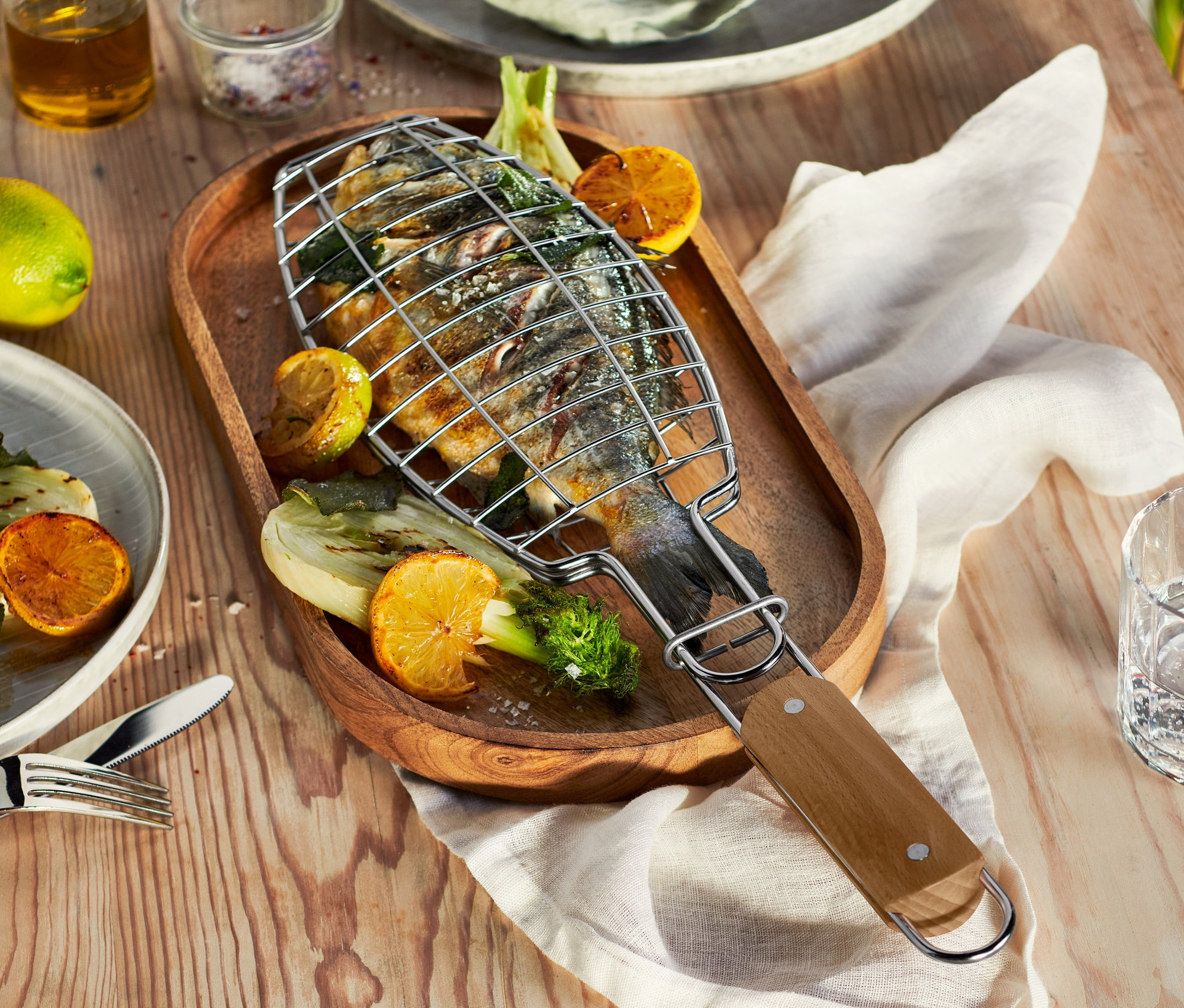 Grilovaná ryba v obracačke na grilovanie rýb na drevenom podnose s citrónom a zeleninou.