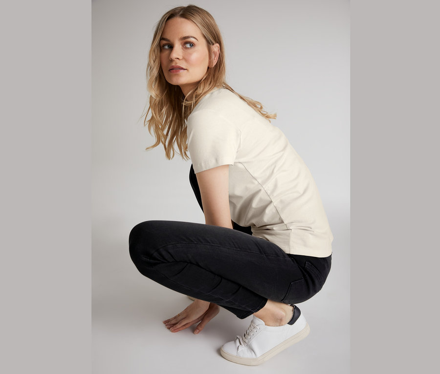 Žena v podrepe má na sebe úzke džínsy, tričko a tenisky.