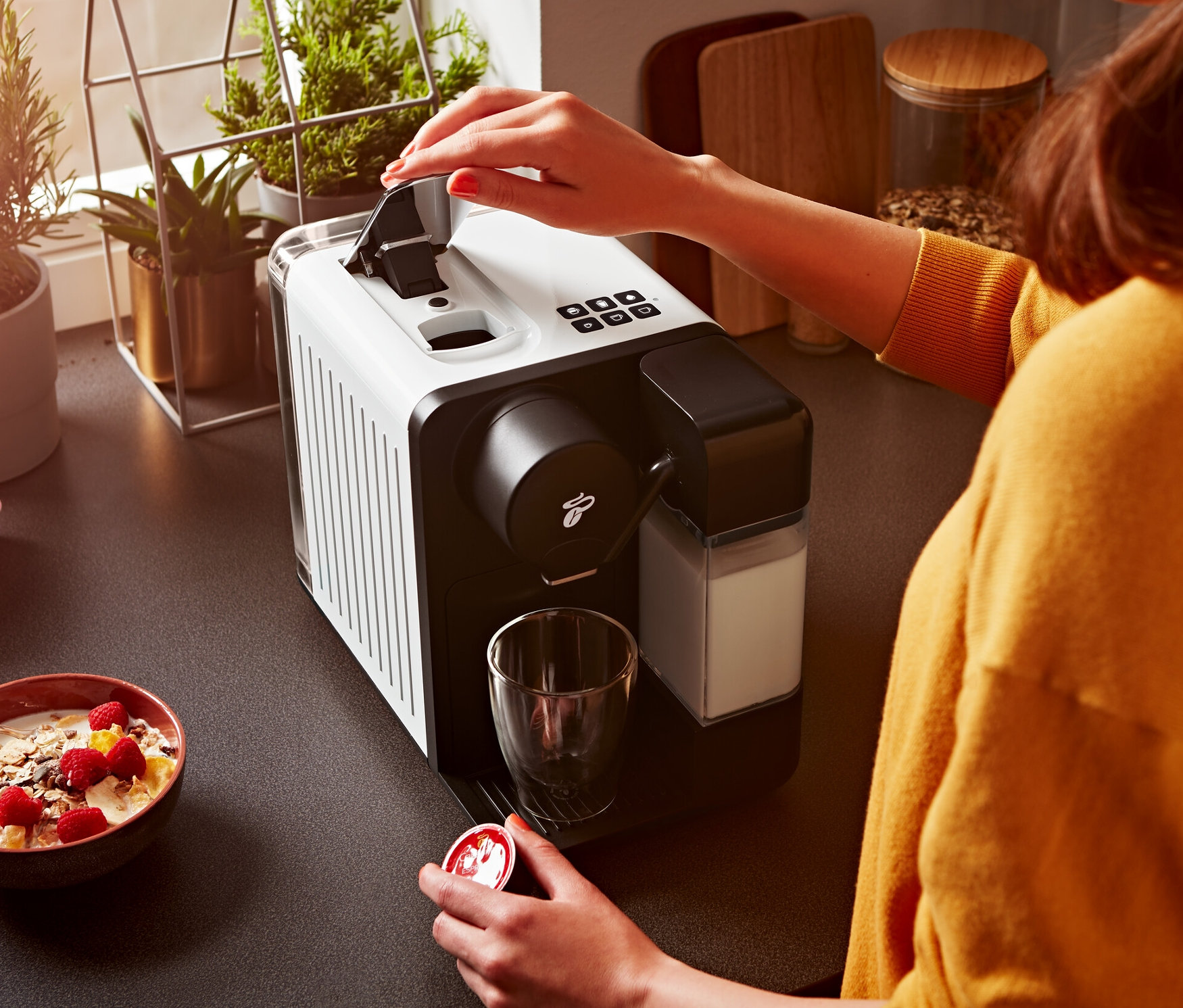 Žena otvára biely kávovar Cafissimo milk a drží kapsulu.