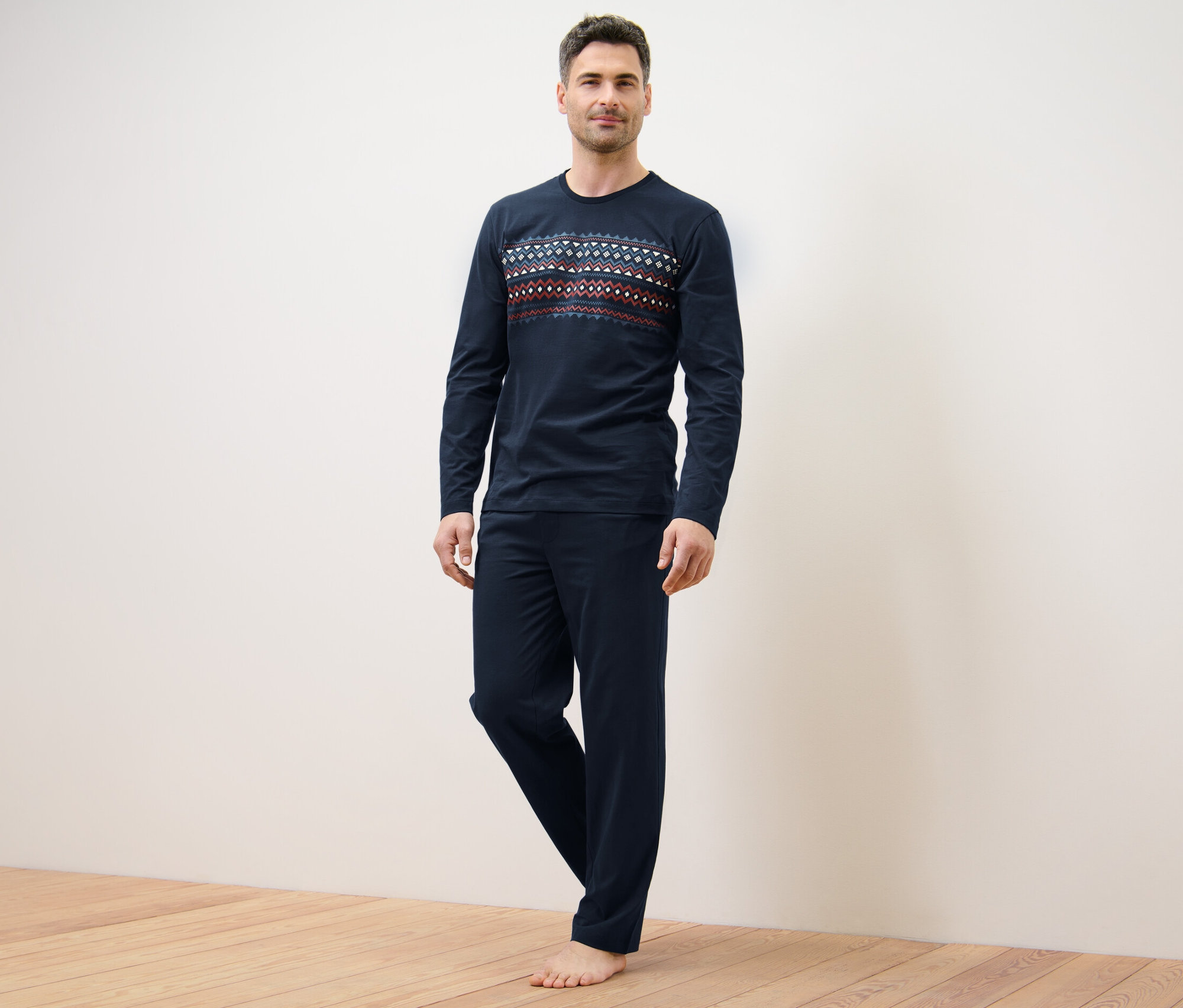 Muž stojí a má na sebe tmavomodré pyžamo s nórskym vzorom.
