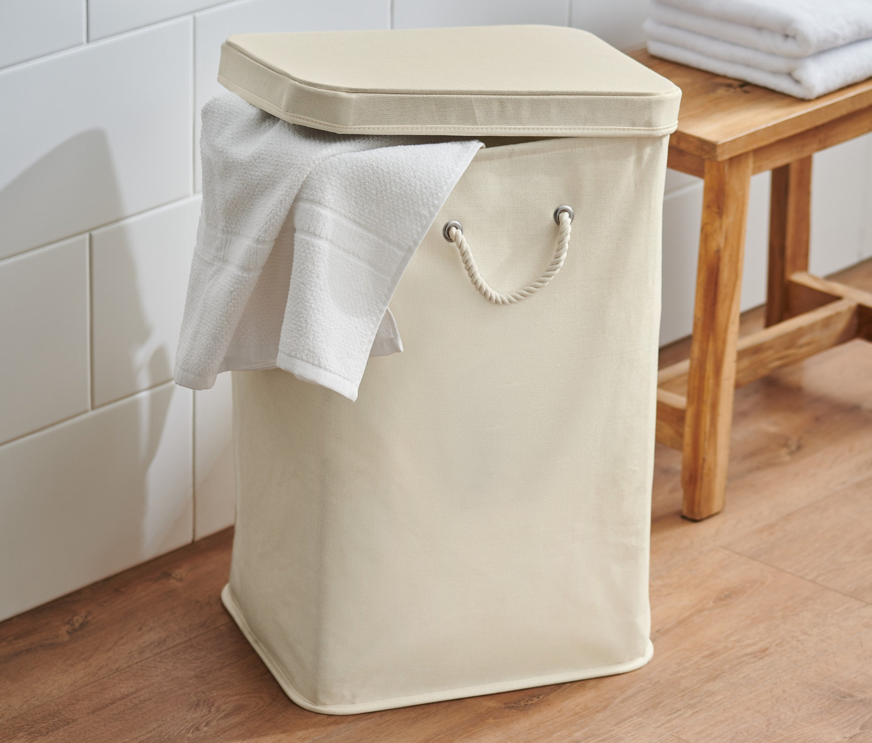 Krémový kôš na bielizeň s vekom a uterákom, stojaci v kúpeľni.