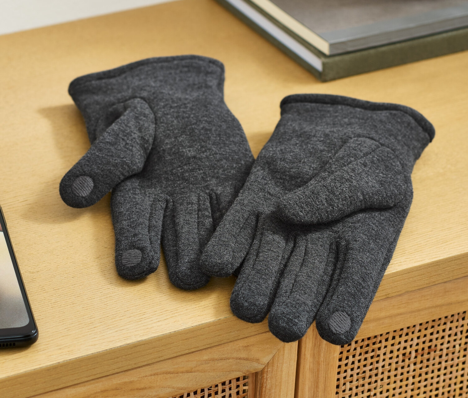 Dvoje rukavice z teplákoviny ležia na drevenej komode vedľa mobilného telefónu.