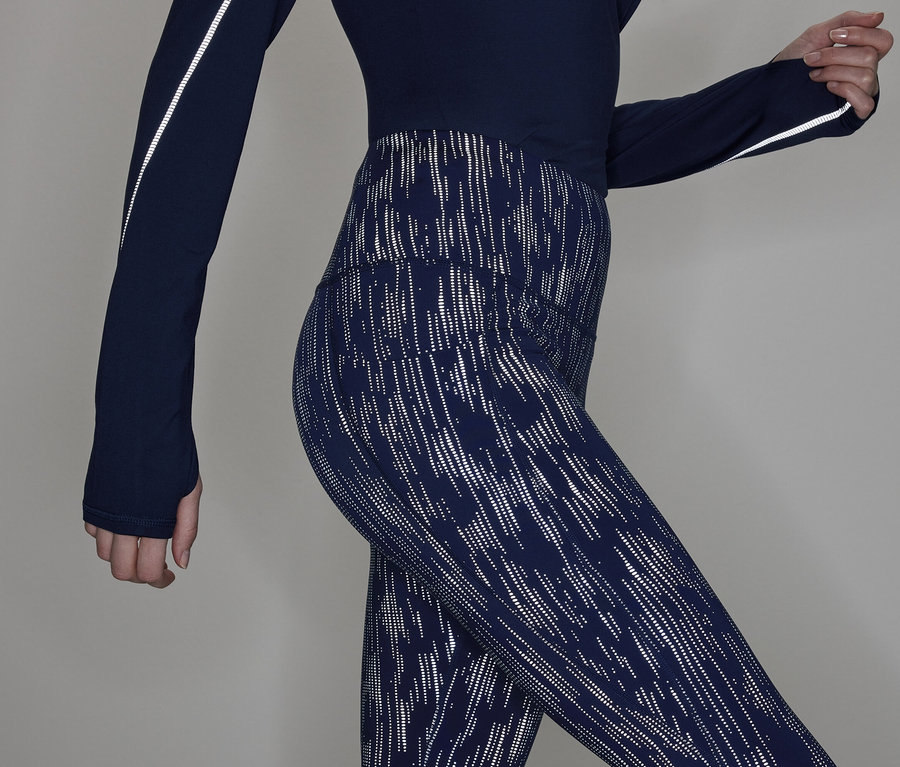 Čiastočný pohľad na ženu v tmavomodrom tope s dlhým rukávom a vzorovaných legínach.