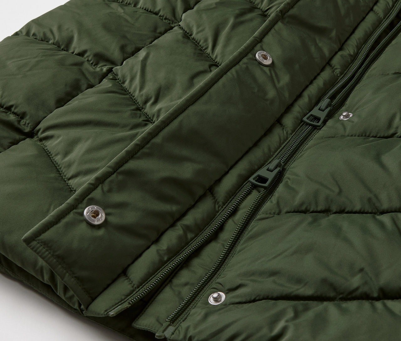 Detailný záber na tmavozelenú prešívanú bundu s kapucňou.