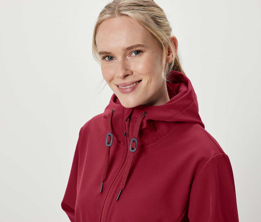 Portrét usmievajúcej sa ženy v bordovej mikine s kapucňou.