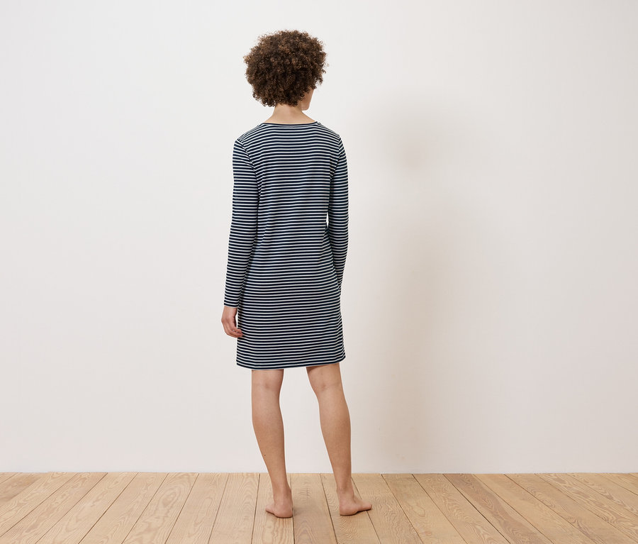 Žena stojí chrbtom k fotoaparátu a má na sebe pruhované šaty.