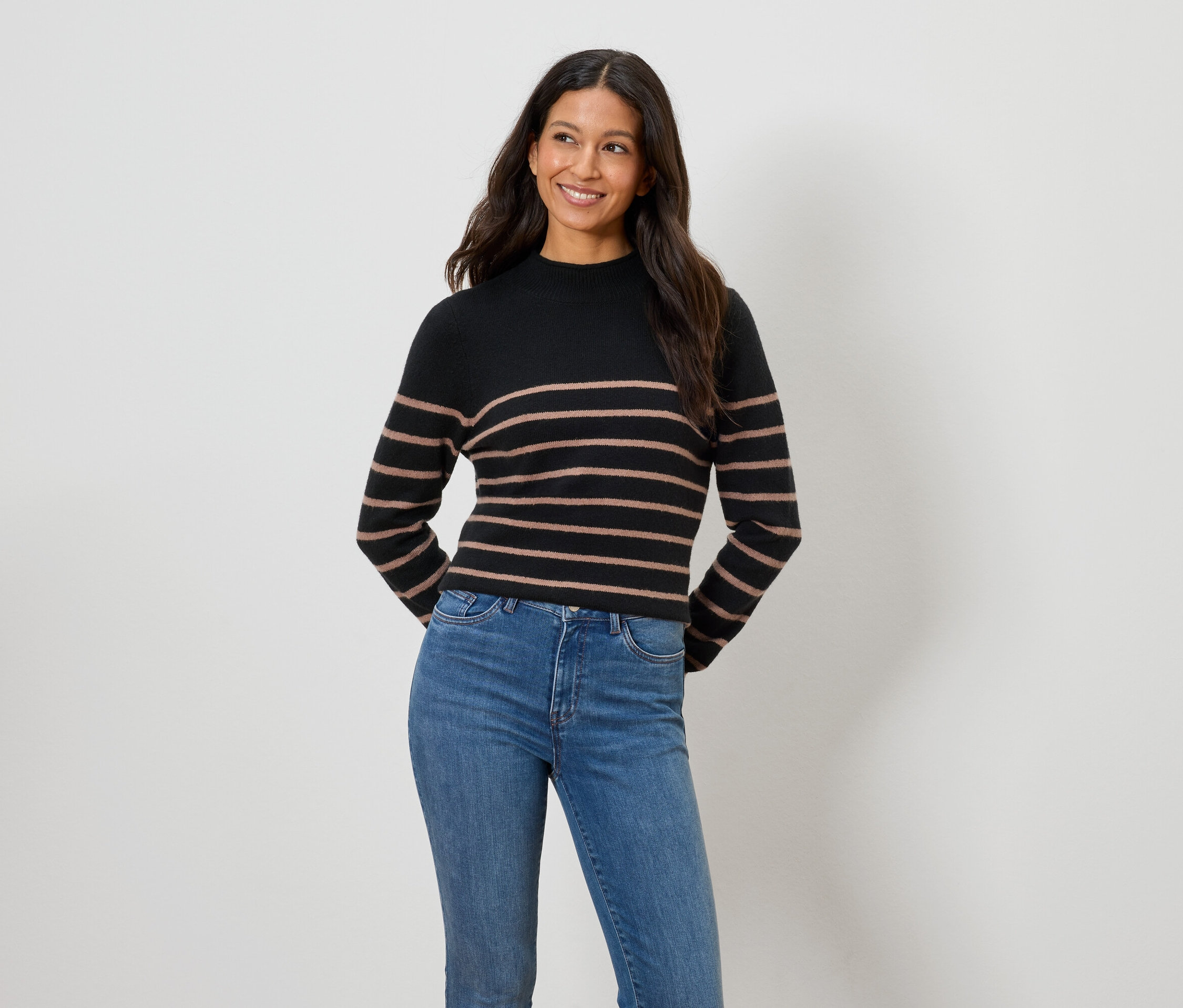 Žena má na sebe čierno-hnedý pásikavý sveter a modré džínsy.