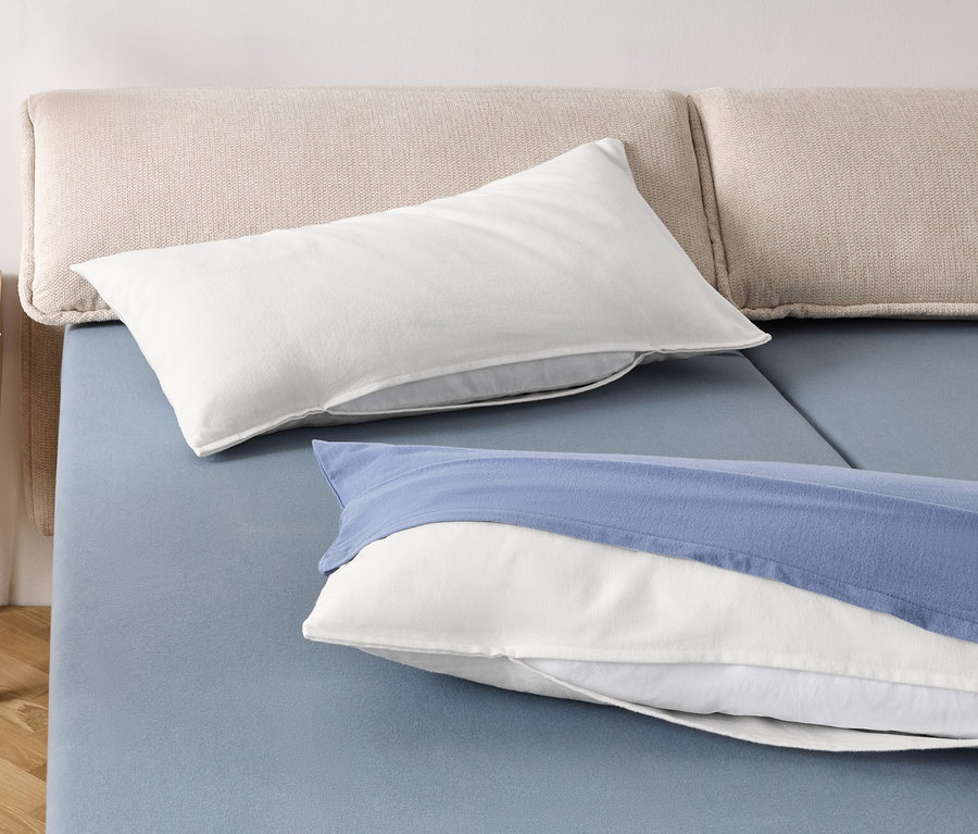 Dva biele vankúše a jeden biely vankúš s modrým obliečkom na modrej posteli.