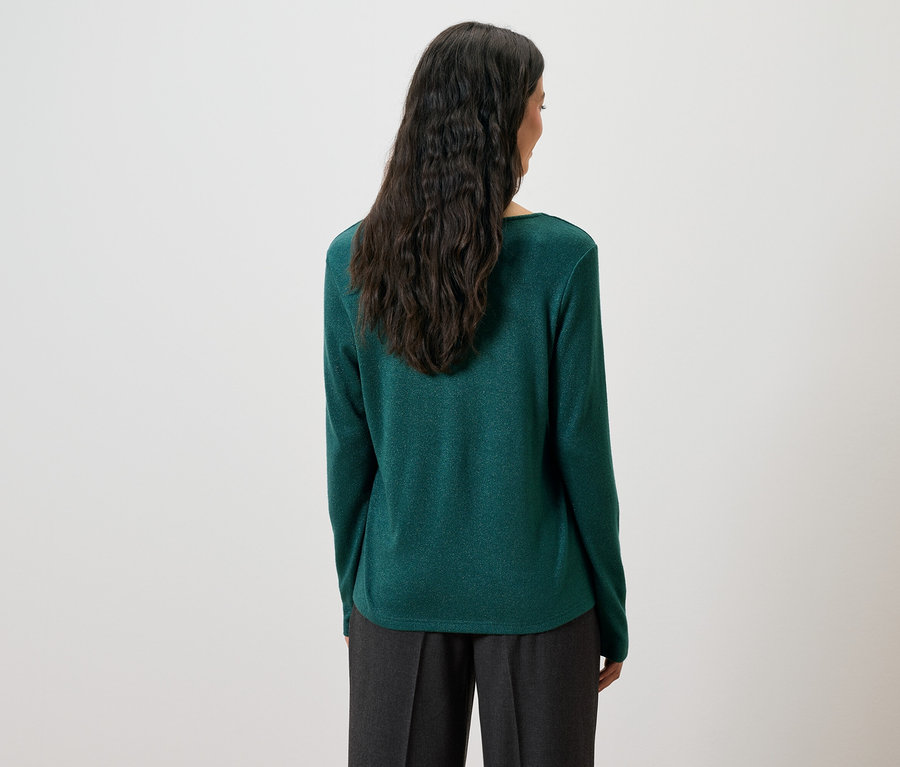 Pohľad zozadu na ženu s dlhými tmavými vlasmi v zelenom svetri a sivých nohaviciach.