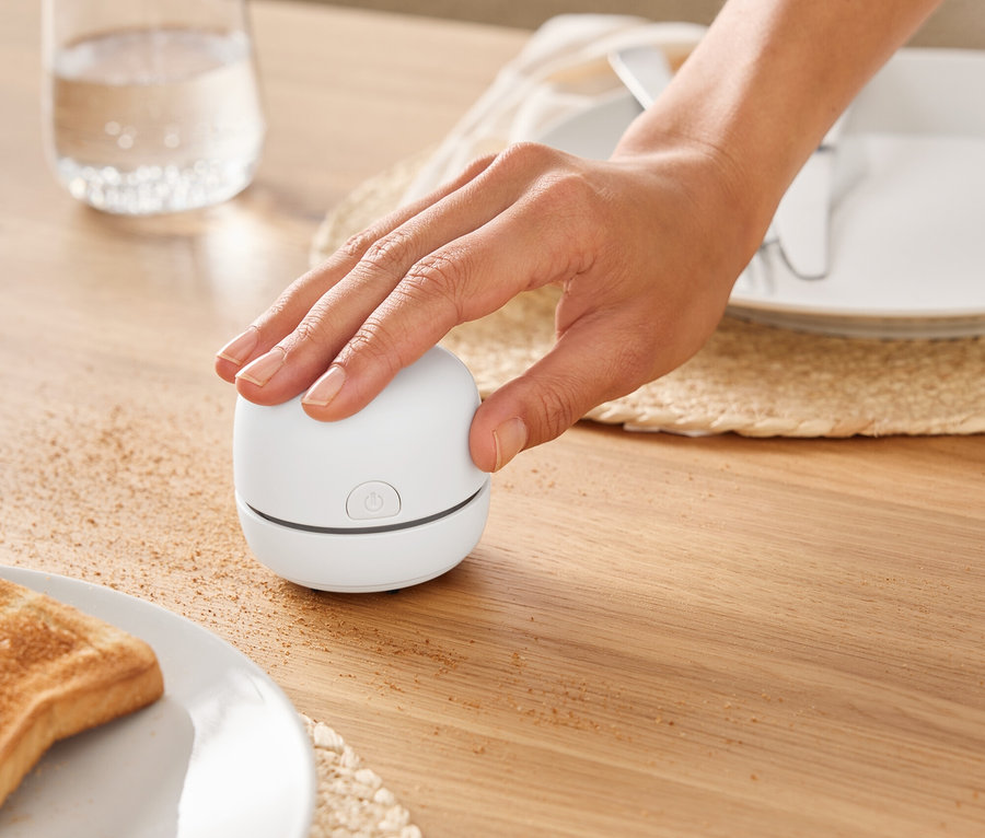 Ruka zapína malý biely spotrebič na drevenom stole vedľa pohára vody.