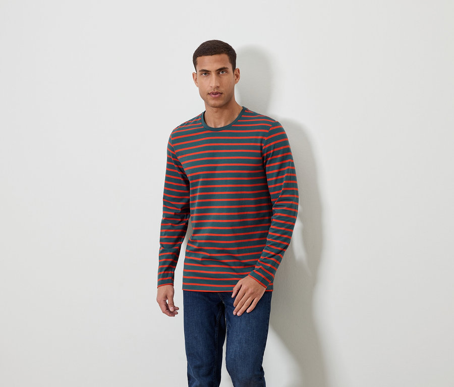 Muž stojí a má na sebe pruhované tričko s dlhým rukávom a džínsy.