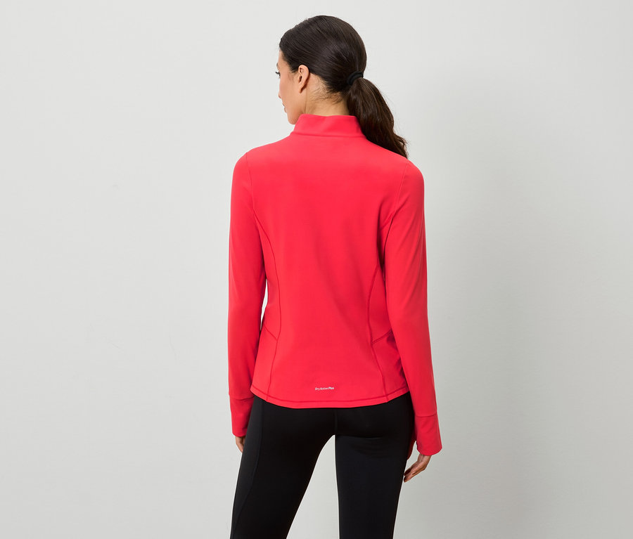 Žena chrbtom k fotoaparátu má na sebe červenú mikinu na zips a čierne legíny.