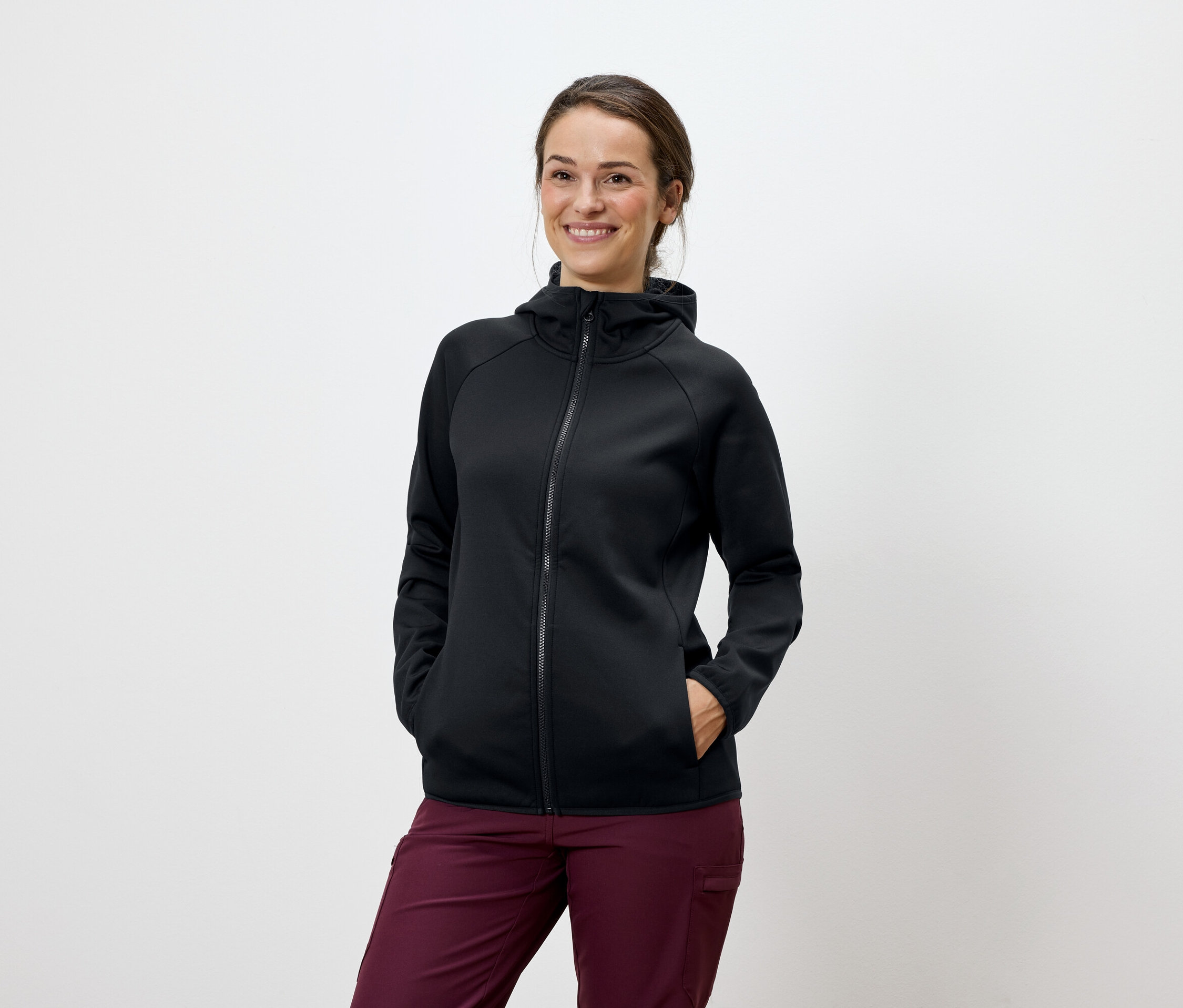 Žena pózuje v čiernej mikine s kapucňou a bordových nohaviciach.