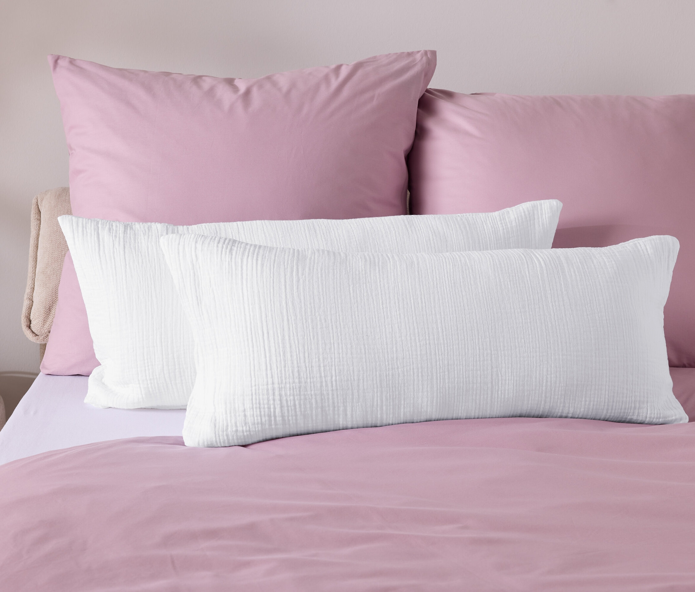 Detail posteľnej bielizne s ružovou prikrývkou a bielymi vankúšmi.