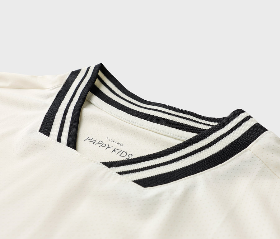 Detailný pohľad na biele tričko s čierno-bielym pruhovaným golierom a logom 'TCHIBO HAPPY KIDS'.