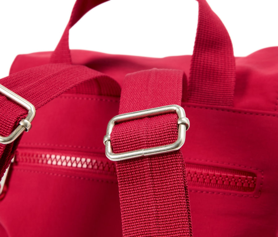 Detailný záber na červený batoh so striebornými prackami na popruhoch.