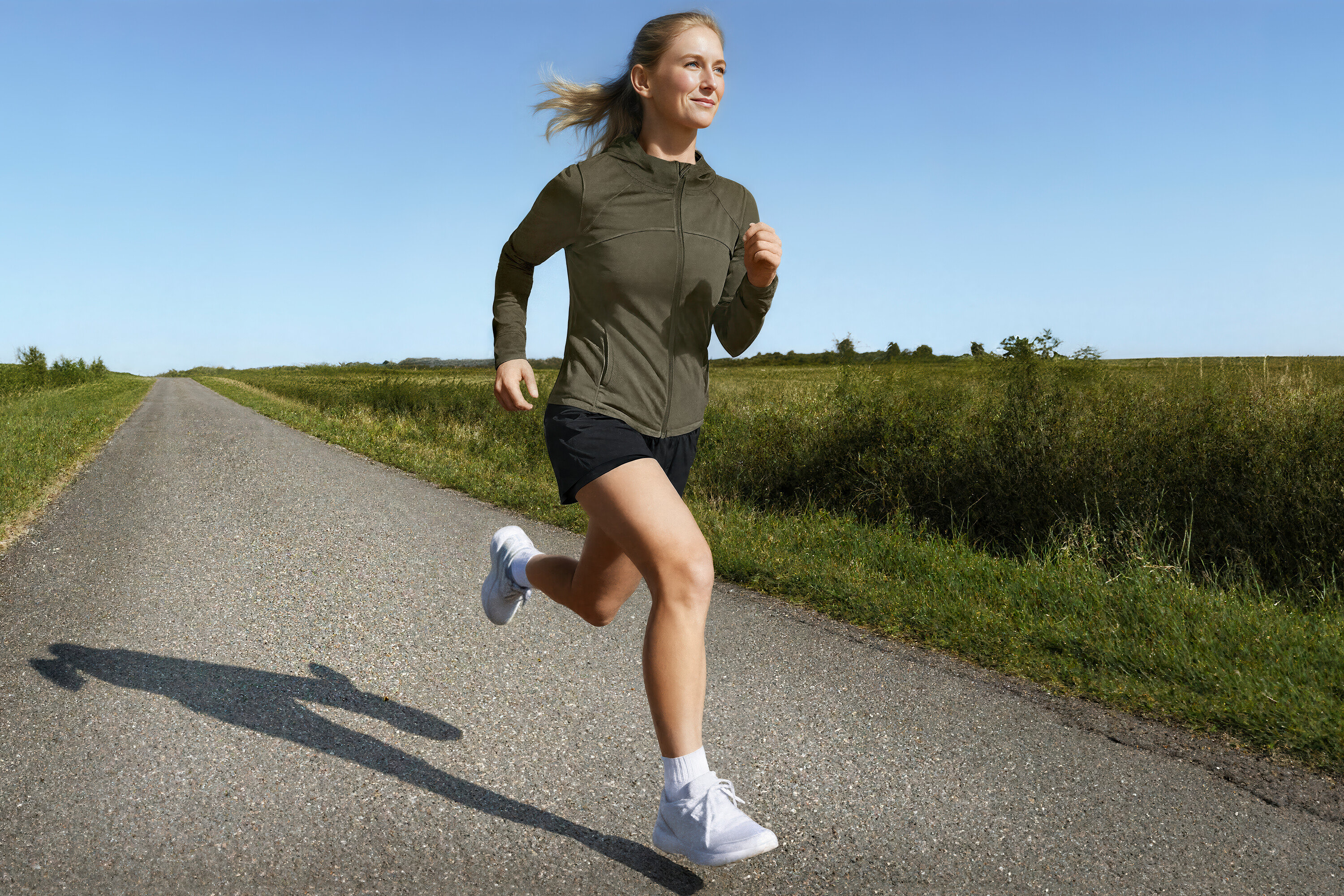 Žena beží v športovej bunde a 2-v-1 bežeckých šortkách po vidieckej ceste.