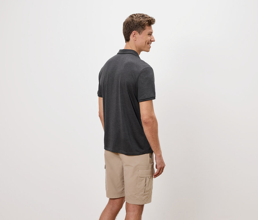 Muž stojí bokom, má na sebe sivé polotričko a béžové cargo šortky na bielom pozadí.