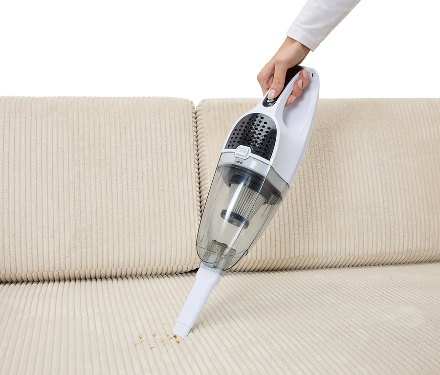 Ruka vysáva omrvinky z béžovej sedačky pomocou 2-v-1 akumulátorového vysávača.