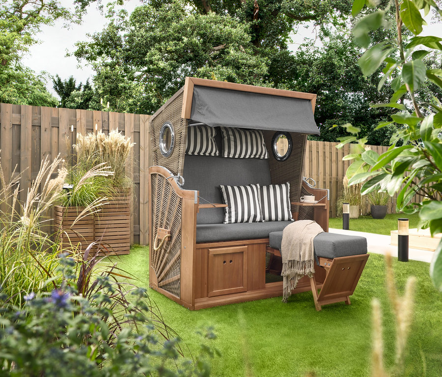 Na tráve stojí plážový kôš Premium XL s 2 výklopnými stolíkmi, vedľa neho 2 stĺpiky na rastliny »Tinus«. V pozadí je vidieť LED solárne bodce na zapichnutie.