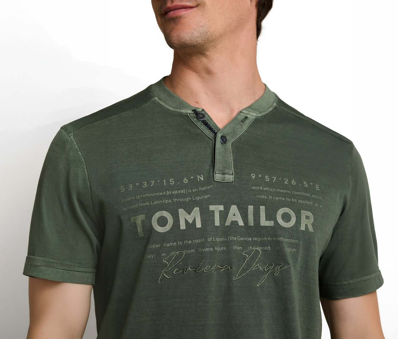 Muž má na sebe zelené tričko s krátkym rukávom a Henley výstrihom. Na tričku sú nápisy „TOM TAILOR“ a „Riviera Days“ a ďalšie popisné texty.