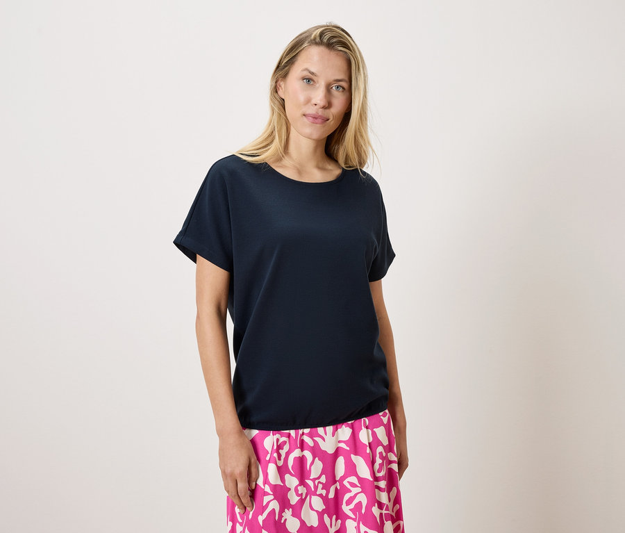 Blondínka má na sebe tmavomodré tričko a ružovo-bielu sukňu na bielom pozadí.