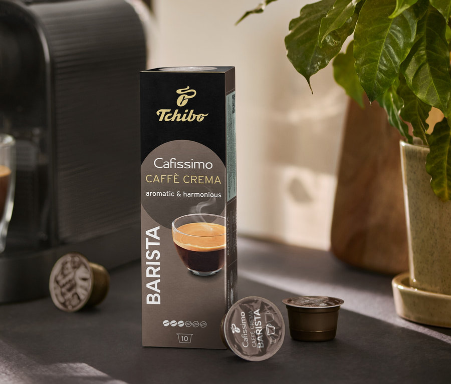 Kávovar plní pohár kávou. Vedľa stojí balenie Cafissimo BARISTA Caffè Crema a niekoľko kapsúl.