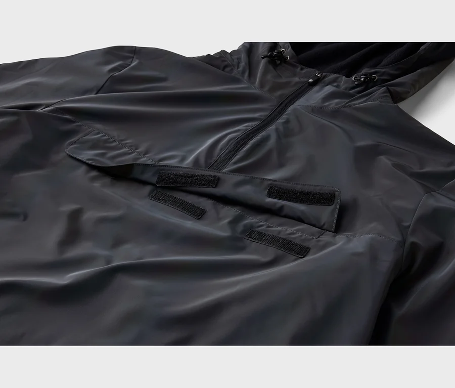 Detail čiernej anorakovej bundy s polovičným zipsom, kapucňou so šnúrkami a veľkým predným vreckom s chlopňou na suchý zips.