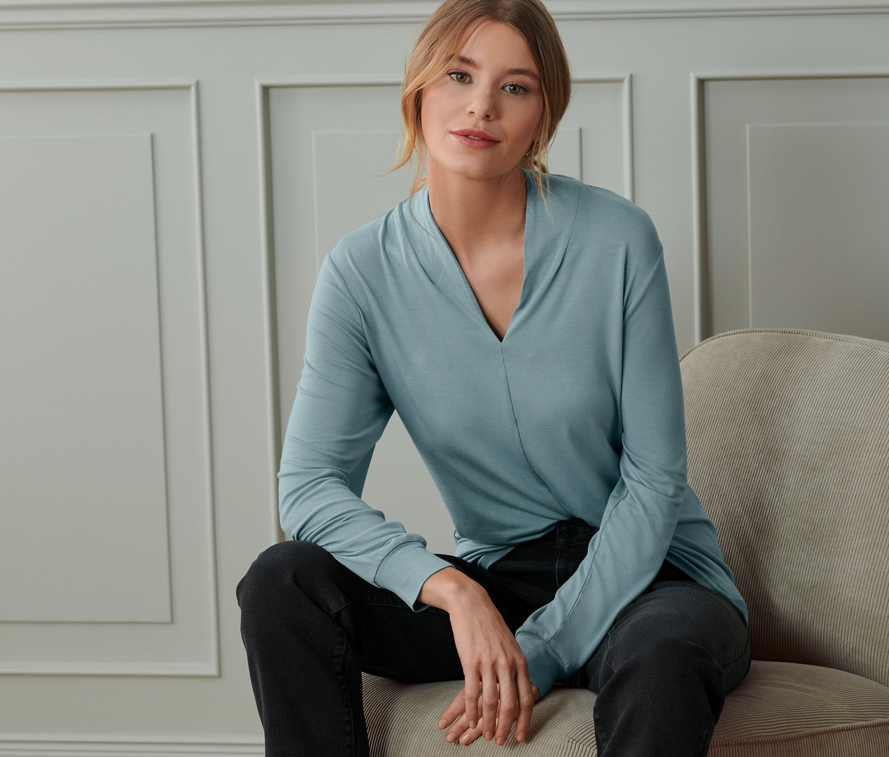 Žena sedí na stoličke a má na sebe dymovomodré tričko s dlhým rukávom a výstrihom do V.