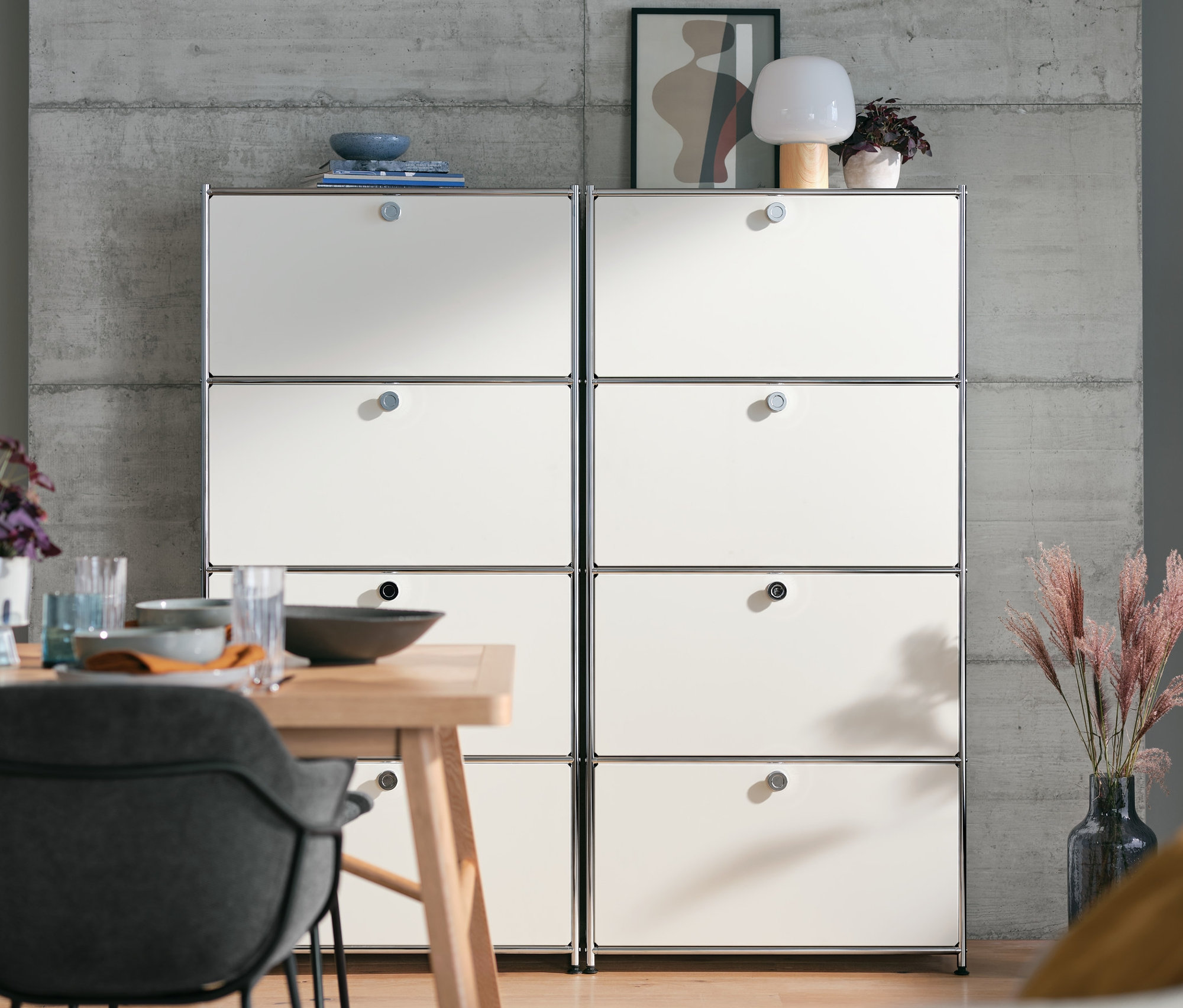 Dve biele kovové vysoké skrinky »CN3« so 4 výklopnými priehradkami stoja vedľa seba za jedálenským stolom.