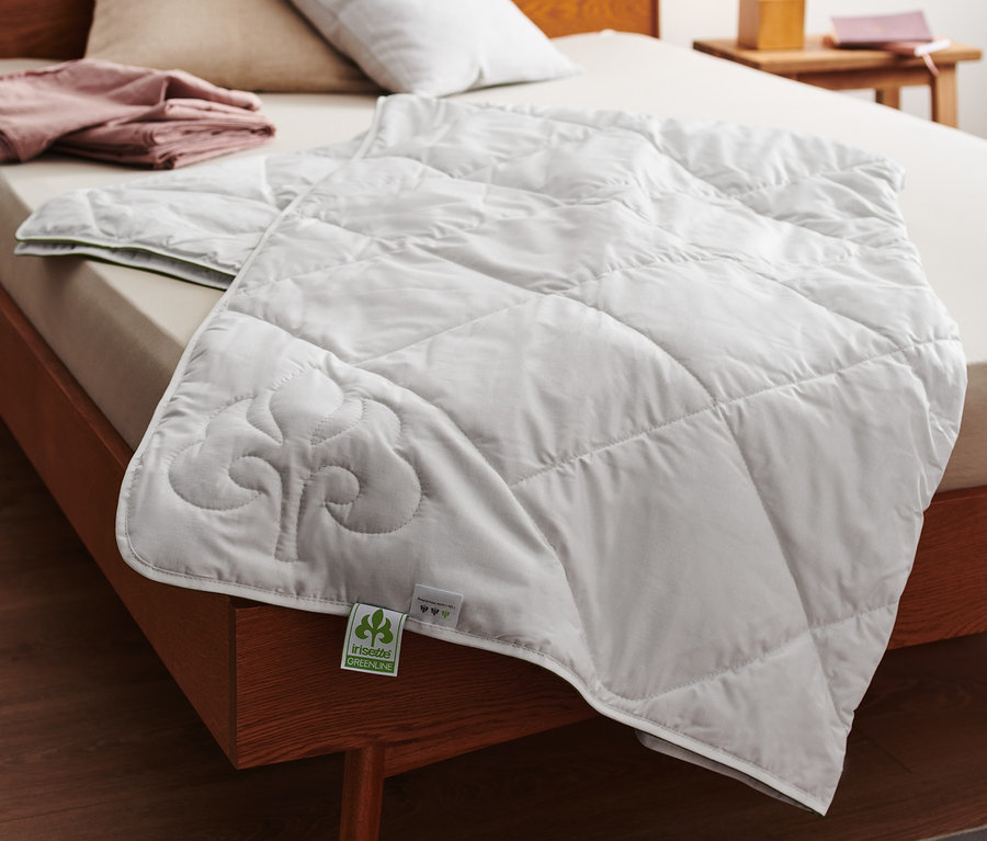 Na posteli leží biela prešívaná prikrývka z bavlny a ľanu irisette® greenline.