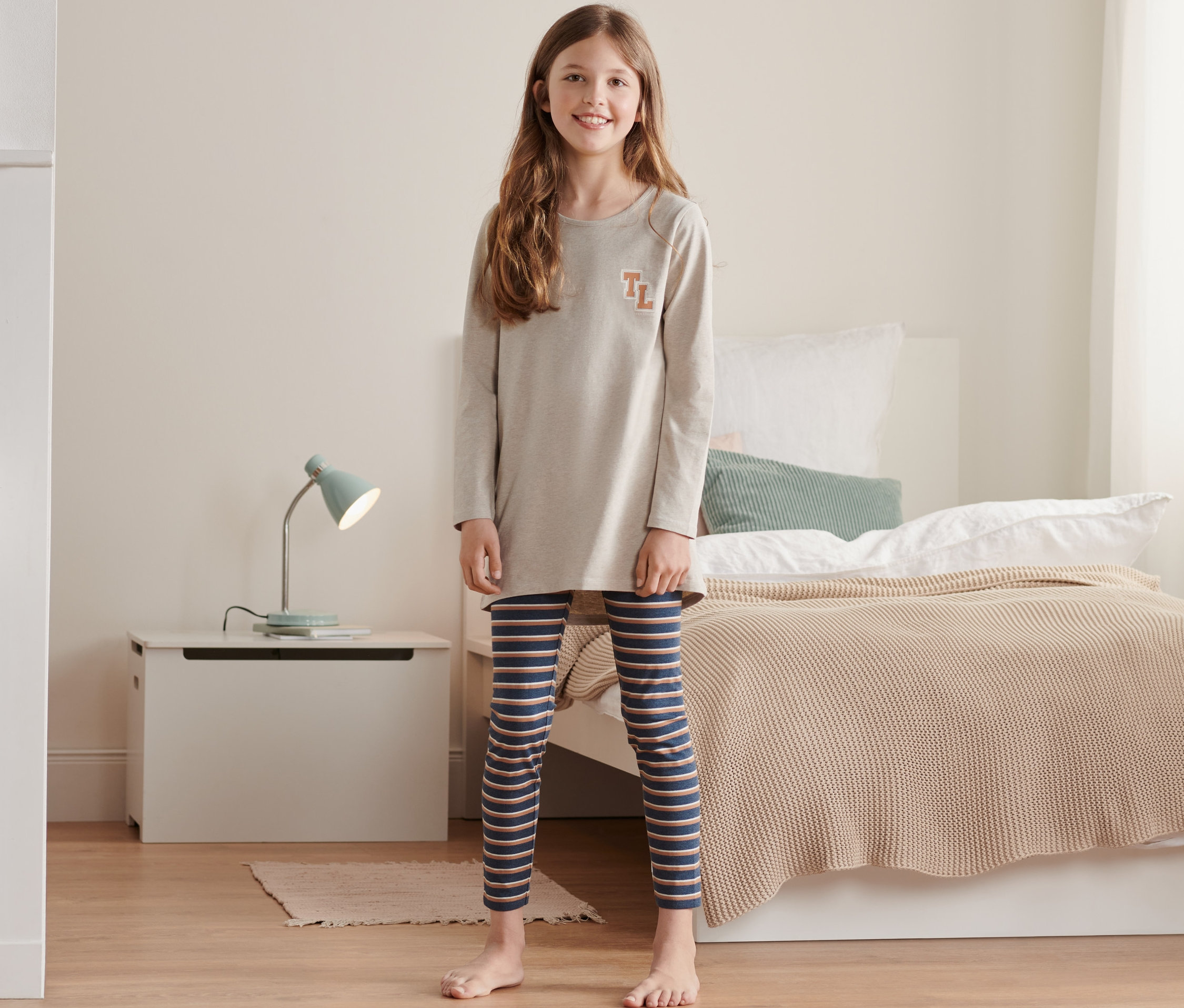 Dievča stojí v detskom pyžame s pruhovanými legínami.