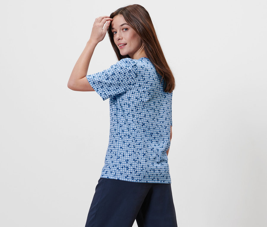 Žena pózuje v modrom blúzkovom tričku s celoplošnou potlačou.