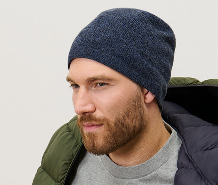 Muž má na sebe pletenú čiapku, tmavomodrú melírovanú, sivý sveter a zelenú páperovú bundu.