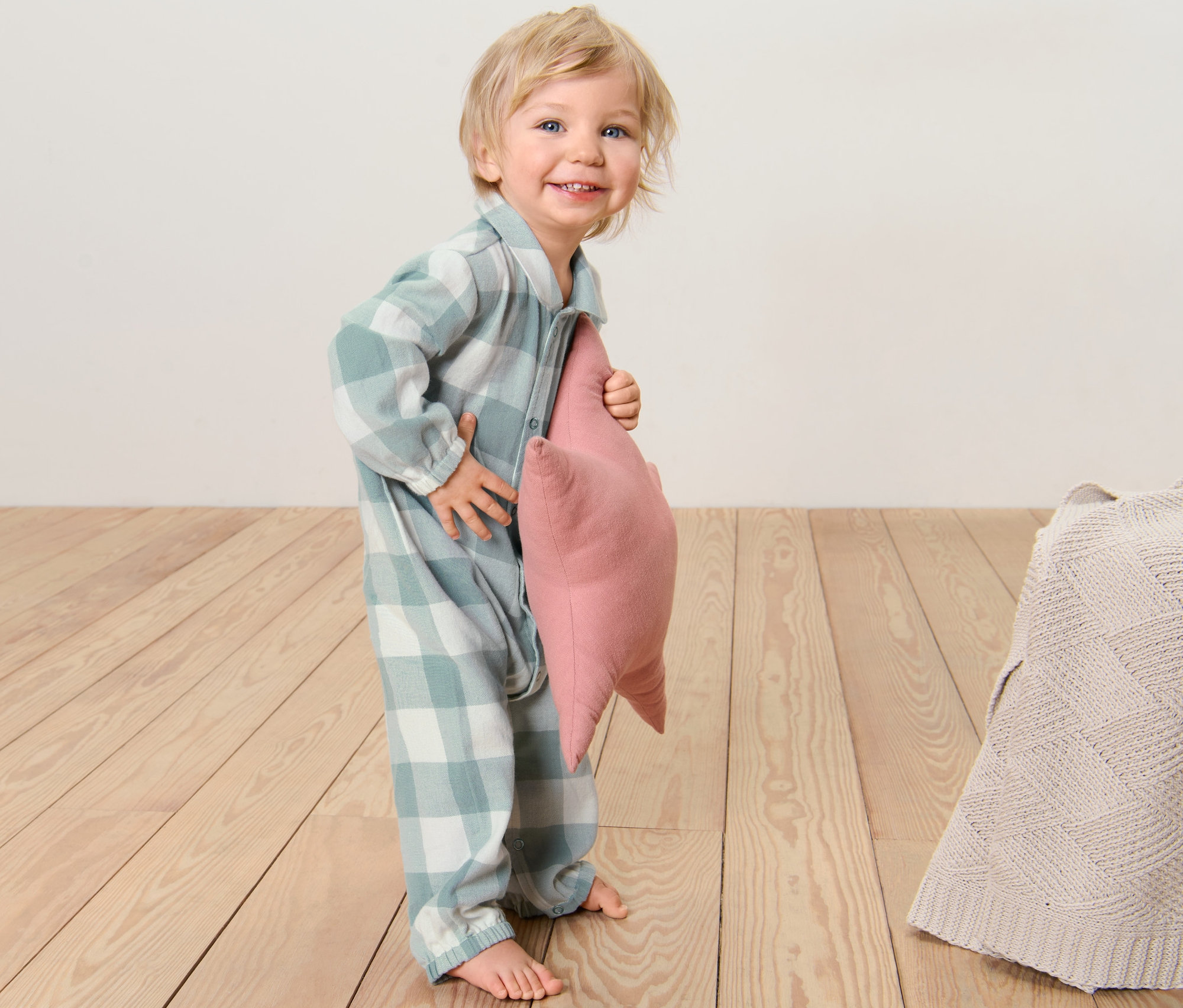 Usmievajúce sa dieťa drží ružový vankúš vo flanelovom dojčenskom pyžame.