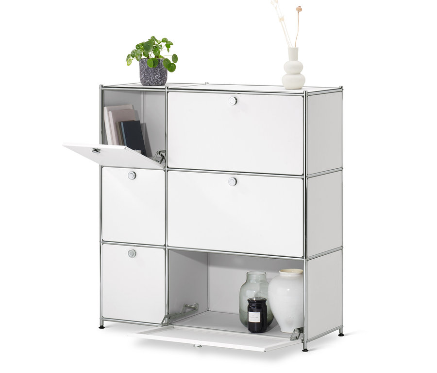 Biela komoda »CN3« so 6 výklopnými dvierkami, z ktorých jedny sú otvorené. Na komode stojí váza s kvetmi a kvetináč.