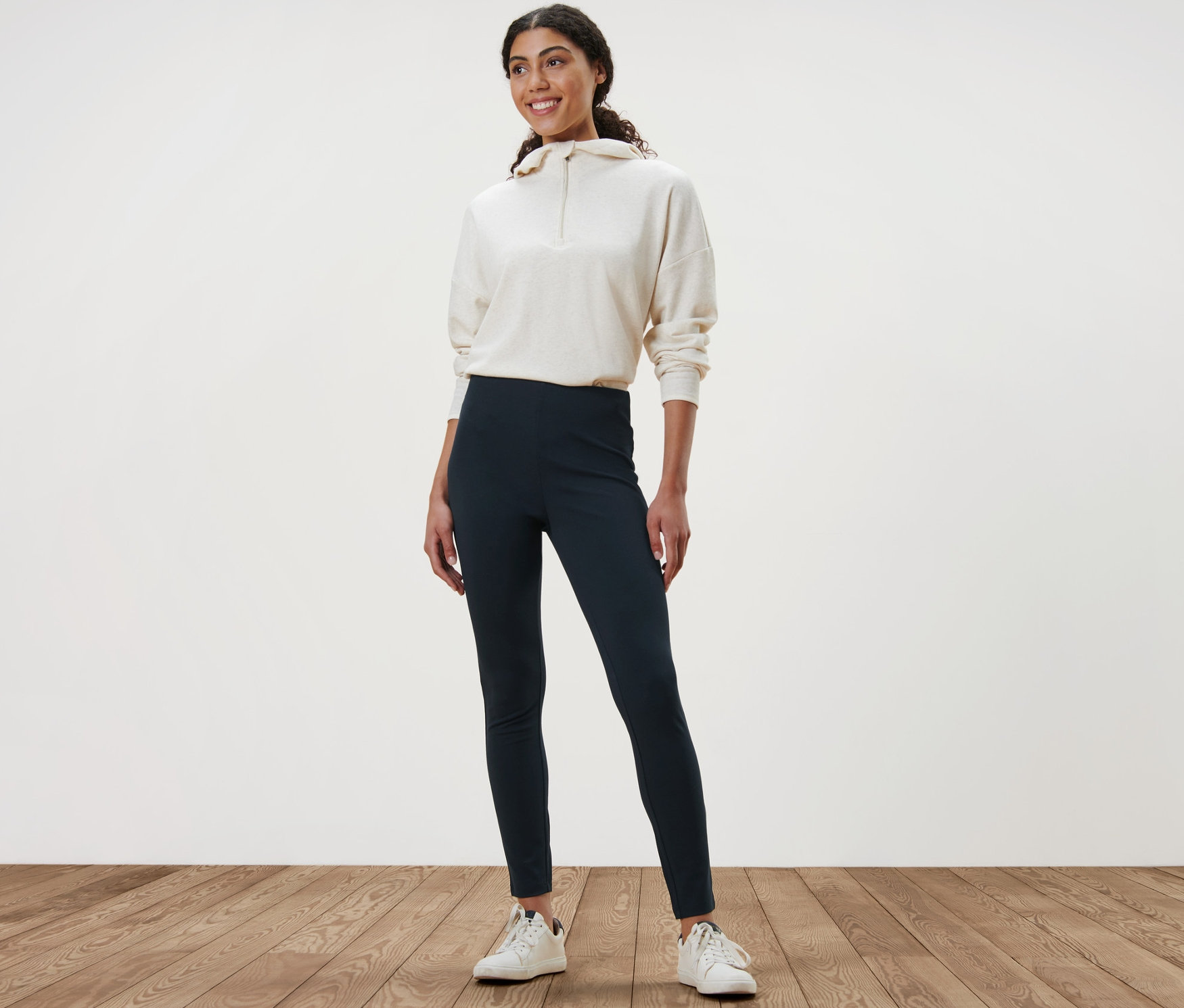 Žena stojaca na drevenej podlahe má na sebe hrubé legínsy a mikinu.